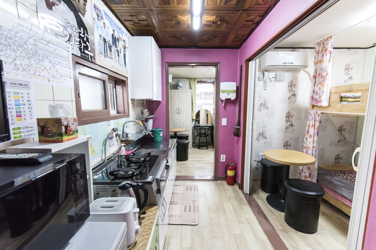 A compact kitchen with a stove, sink, and microwave. There is a small dining area with a table and chairs. The room has purple walls and a wooden ceiling.
