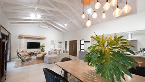 A spacious living area with a large dining table, a sofa, and a TV mounted on the wall. - Bushwillow Private Villa (Hoedspruit)