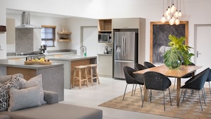 A modern kitchen with a central island, built-in appliances, and a dining area with a wooden table and chairs. - Bushwillow Private Villa (Hoedspruit)