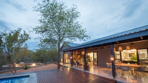 A modern outdoor patio with a pool, wooden deck, and a dining area with outdoor furniture. - Bushwillow Private Villa (Hoedspruit)