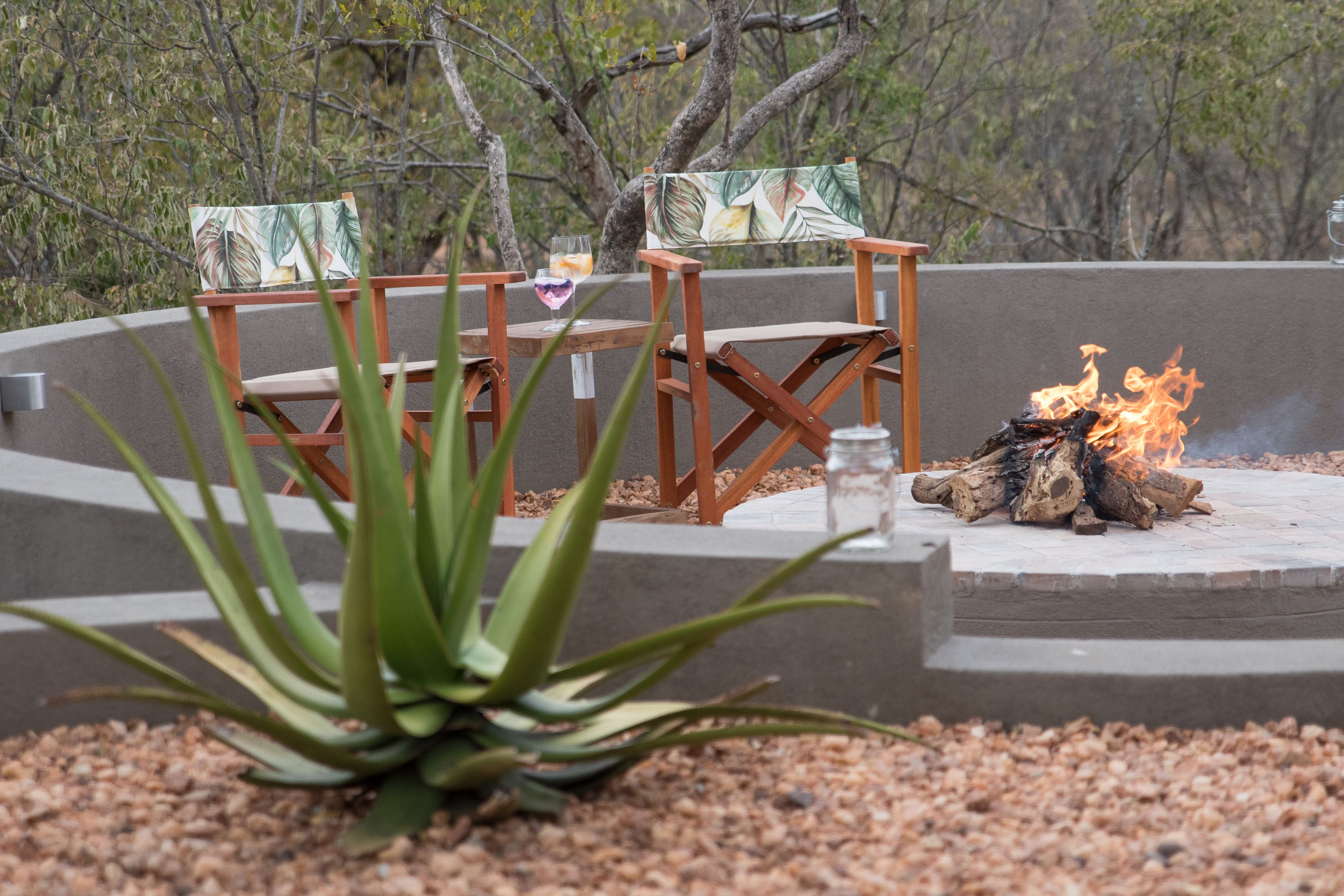 A fire pit with chairs and a table, surrounded by pebbles and plants.