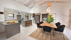 A modern kitchen with a central island, dark wicker chairs, and a wooden dining table. - Bushwillow Private Villa (Hoedspruit)