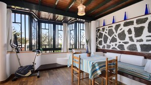 Une pièce avec un plancher en bois, une table recouverte d’une nappe à rayures, un banc, un mur avec un motif en pierre et une fenêtre avec des rideaux.