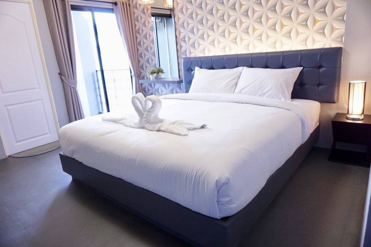 Una cama bien hecha con sábanas blancas y una toalla doblada en forma de corazón.