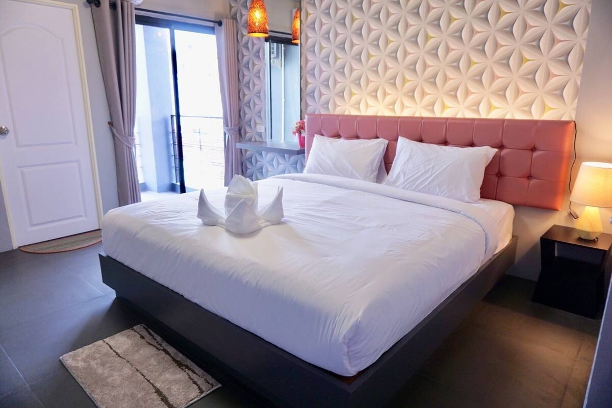 Una habitación de hotel con una cama grande, un adorno en la pared, una mesita de noche y una puerta.
