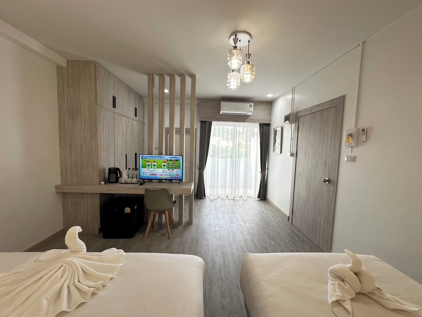 A hotel room with two beds, a desk with a computer, a TV, and a window with curtains.