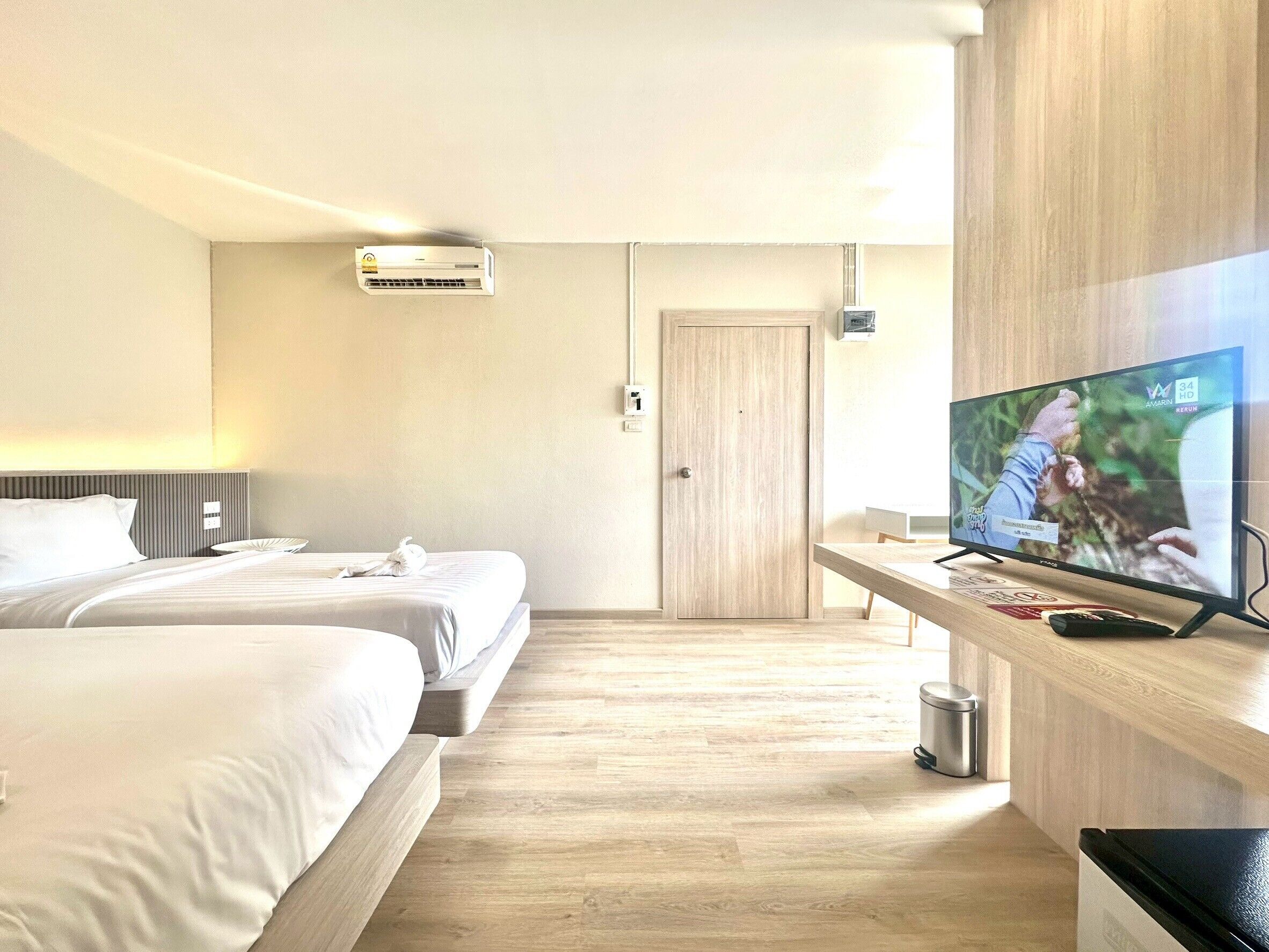 Een hotelkamer met twee bedden, een televisie, een houten vloer en een deur.