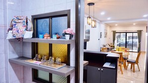 A modern kitchen with a built-in oven, a dining area with a table and chairs, and a view of the outside through a large window. - Bhundaree Richy (Hat Yai)