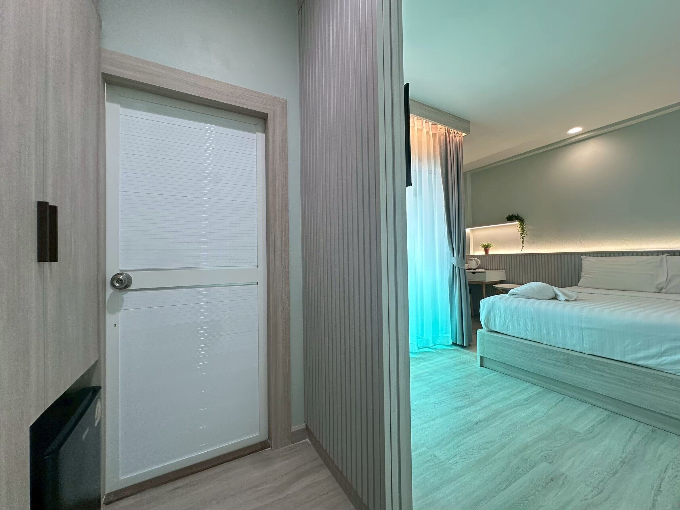 A hotel room with a bed, bedside table, lamp, and a view of the hallway.