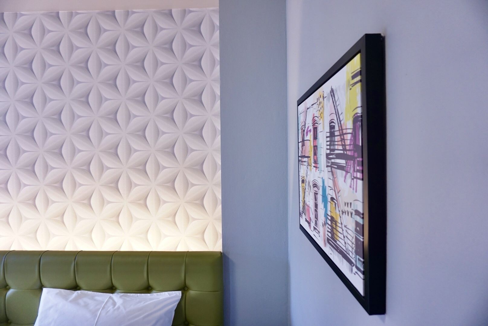 A room with a green upholstered headboard, a textured wall panel, and a framed abstract painting.