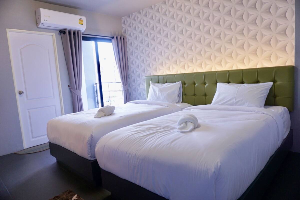 Habitación de hotel con dos camas, un cabecero tapizado en verde, ropa de cama blanca y un papel tapiz estampado.