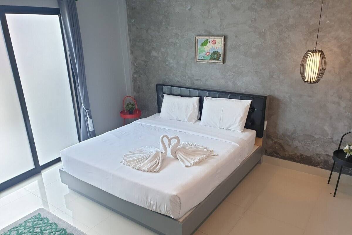 Habitación de hotel moderna con una cama grande, una pared gris con textura, una obra de arte floral enmarco y una lámpara colgante.