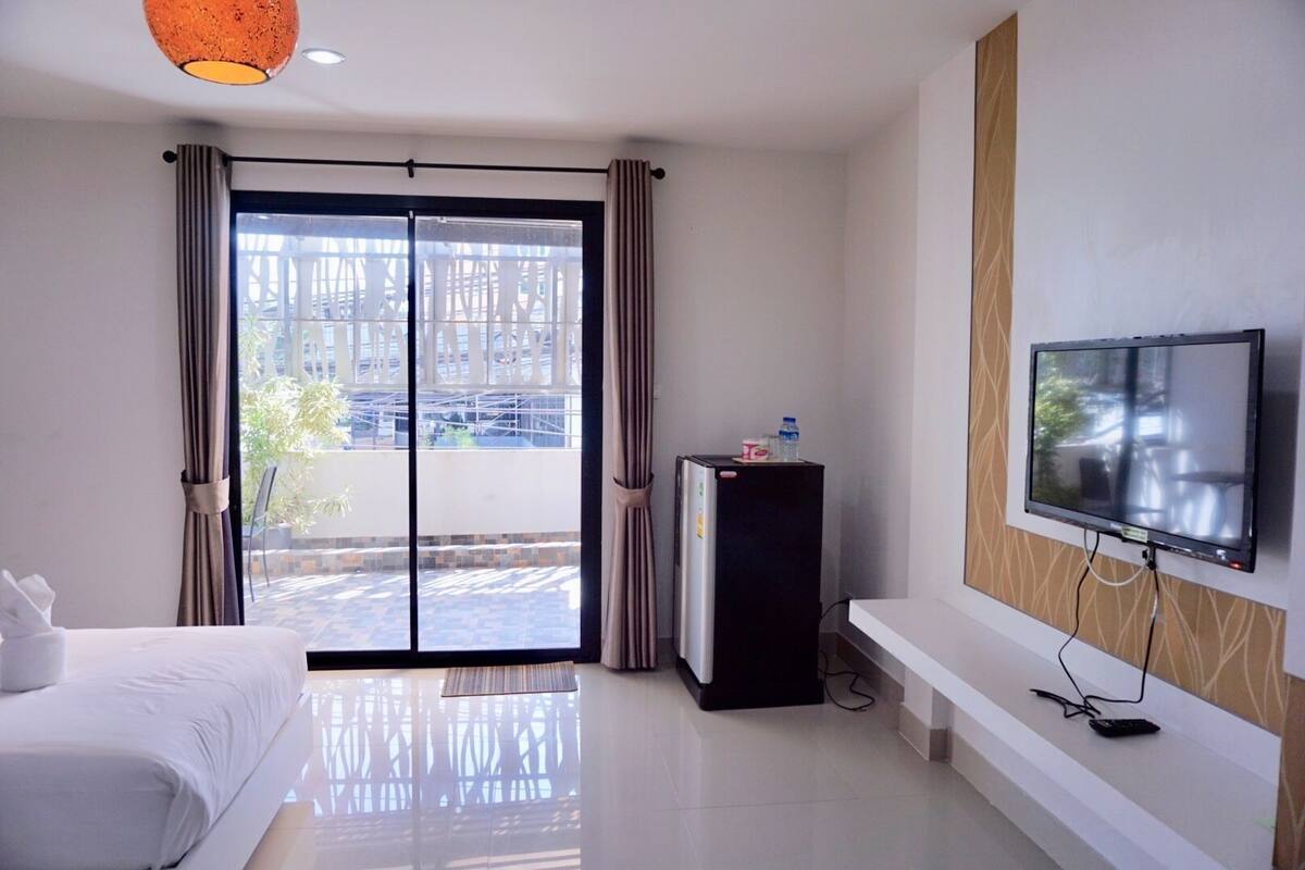 Una habitación de hotel con una cama, un televisor, un refrigerador y un gran ventanal corredizo al exterior.
