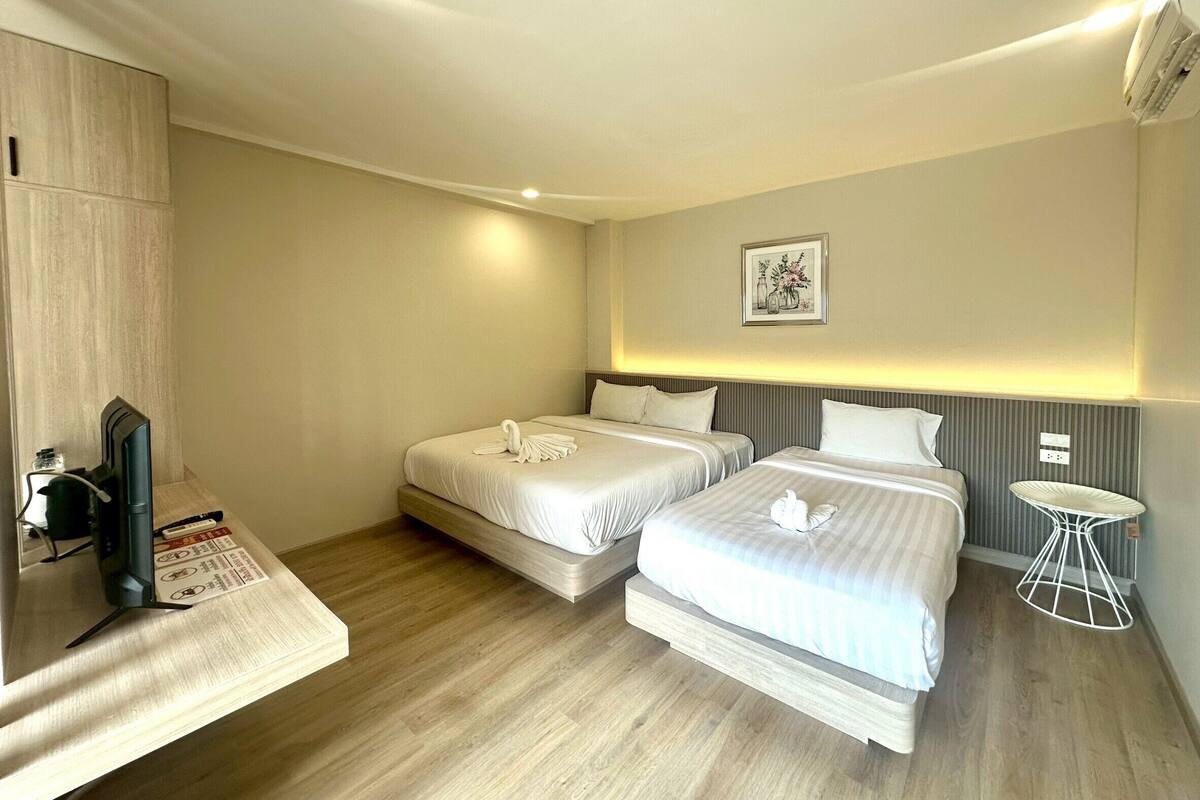 Una habitación de hotel con dos camas, una mesita, un televisor y un cuadro en la pared.