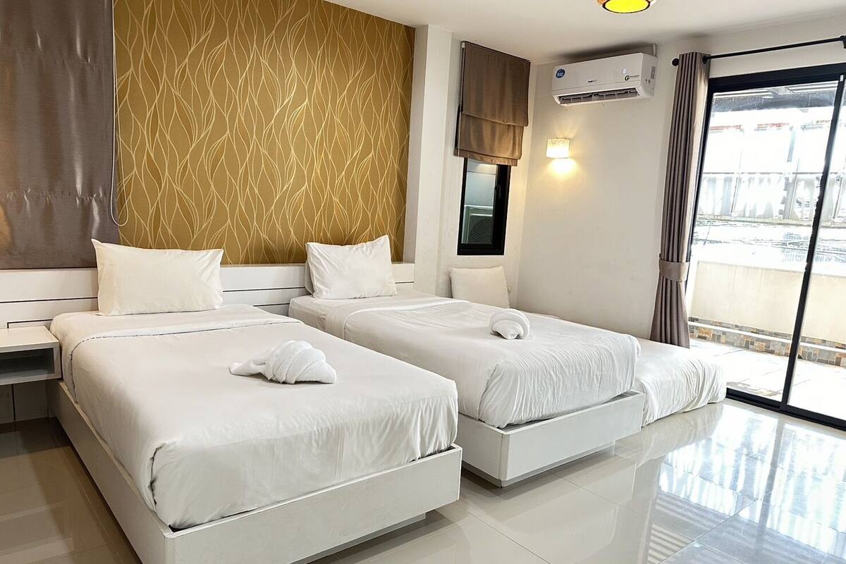 Habitación de hotel con dos camas, ventana con vistas, aire acondicionado y pared con diseño de hojas.