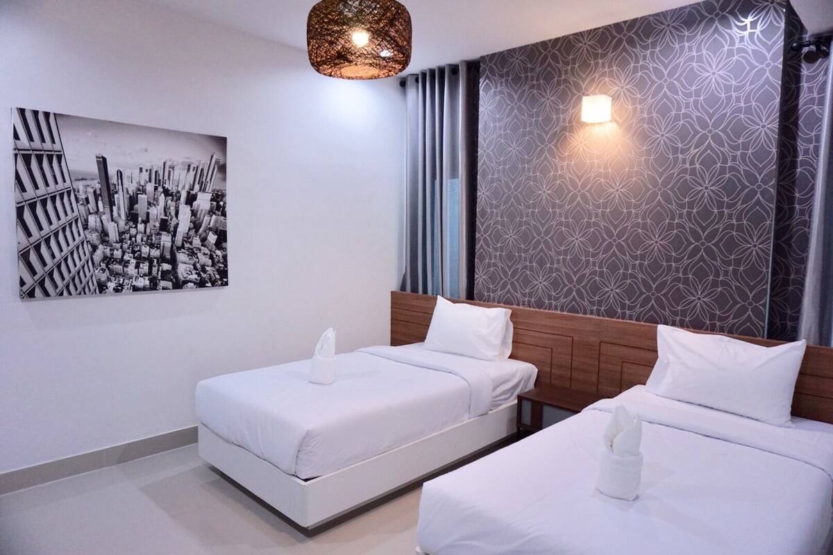 Habitación de hotel moderna con dos camas, una obra de arte con un paisaje urbano, un papel tapiz estampado y una lámpara colgante.