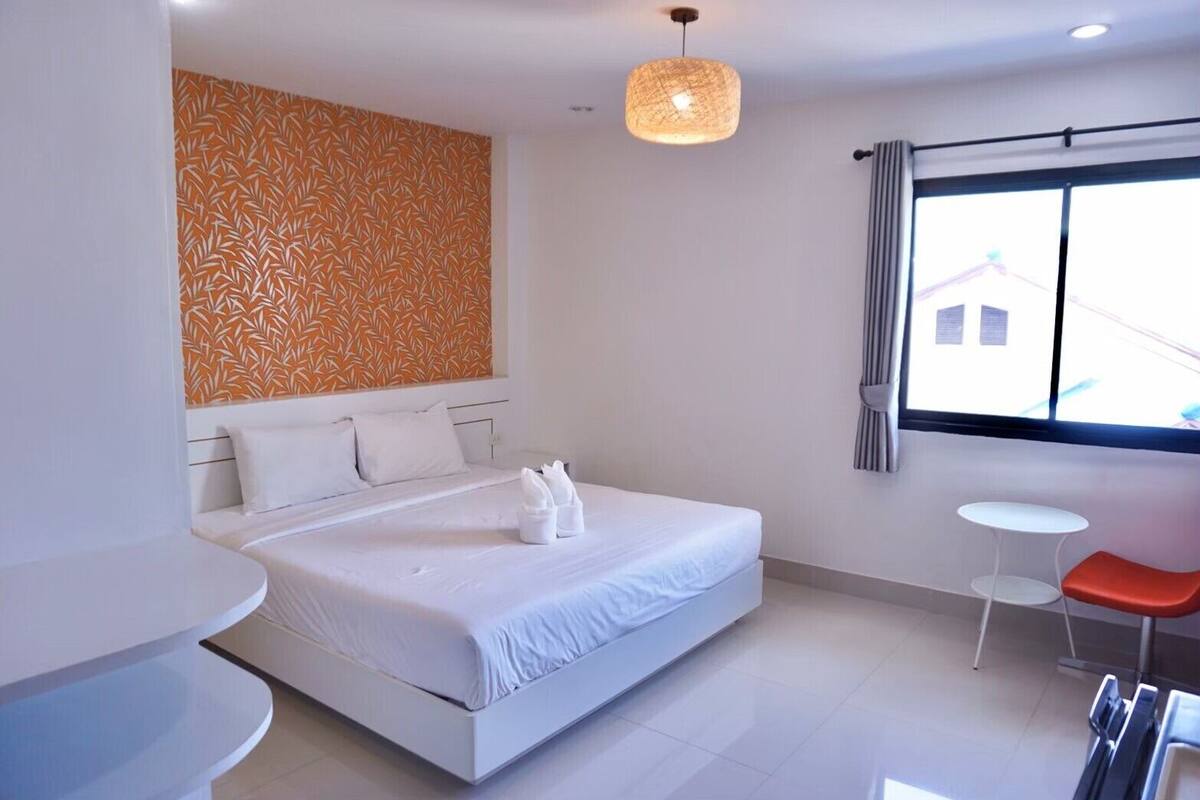 Una habitación de hotel moderna con una cama grande, una mesita redonda y una ventana con cortinas.