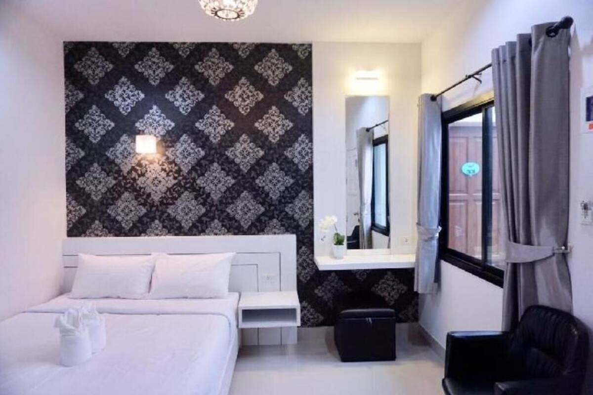Habitación de hotel con cama, mesita de noche, espejo, ventana con cortinas y pared con papel tapiz estampado.
