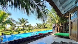 A pool area with a clear view of the pool, a lounge chair, and a wooden table. - Mermaid Beach Resort (Cox's Bazar)