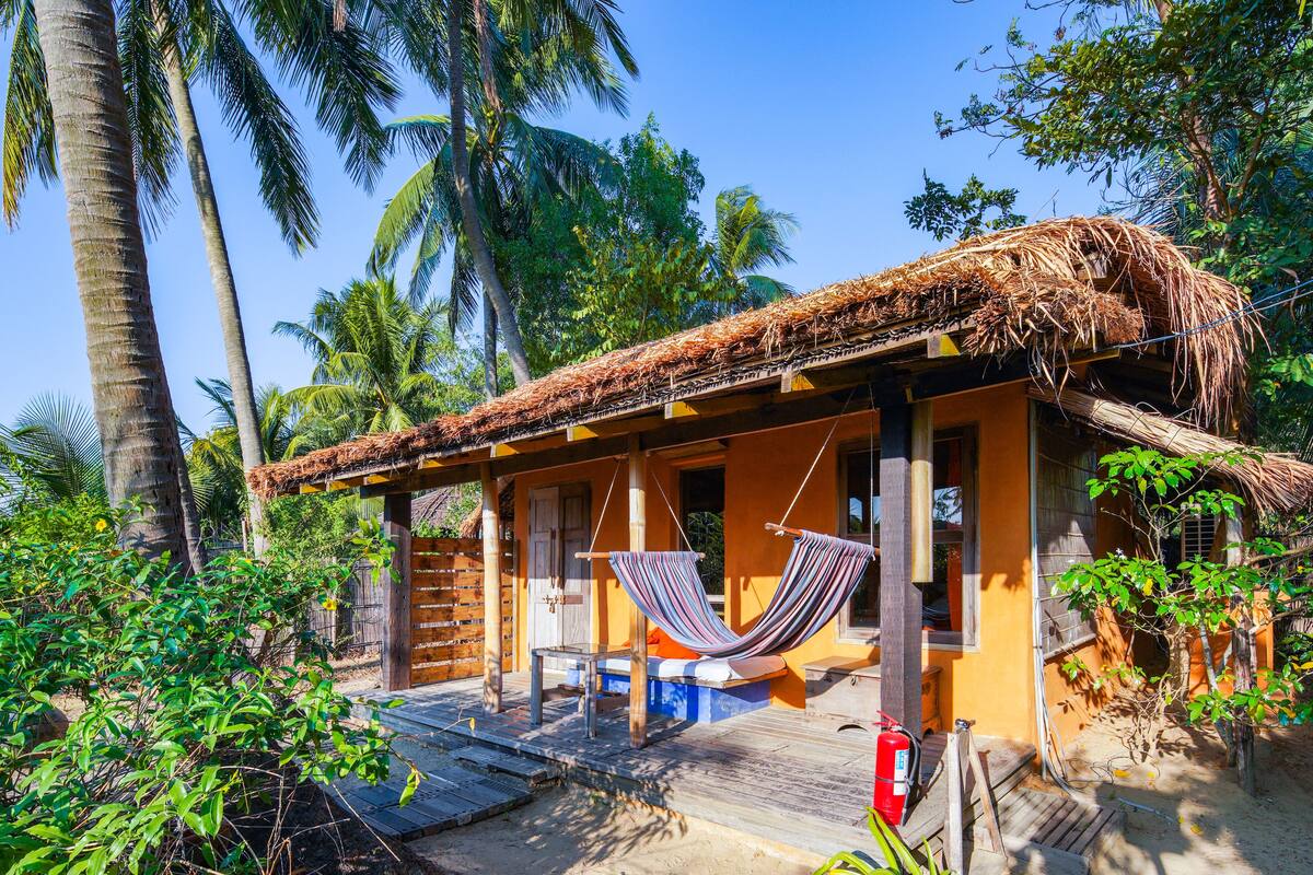 A rustic house with a thatched roof, a hammock, and a wooden deck.