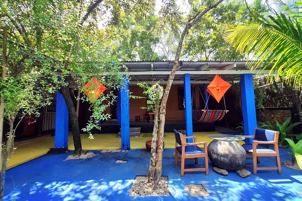An outdoor patio area with blue flooring, wooden chairs, a hammock, and decorative orange diamond-shaped items.