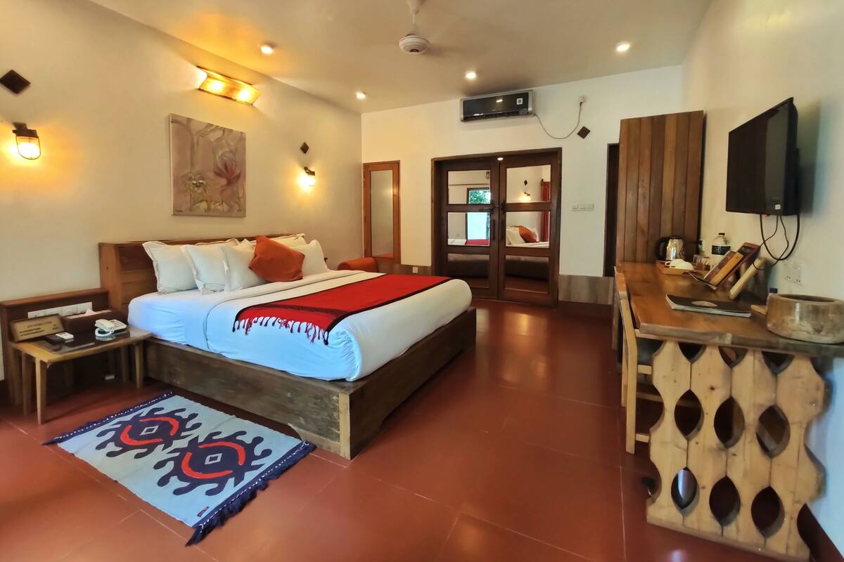 A hotel room with a large bed, bedside tables, a TV, a wooden cabinet, and a red and white bedspread.