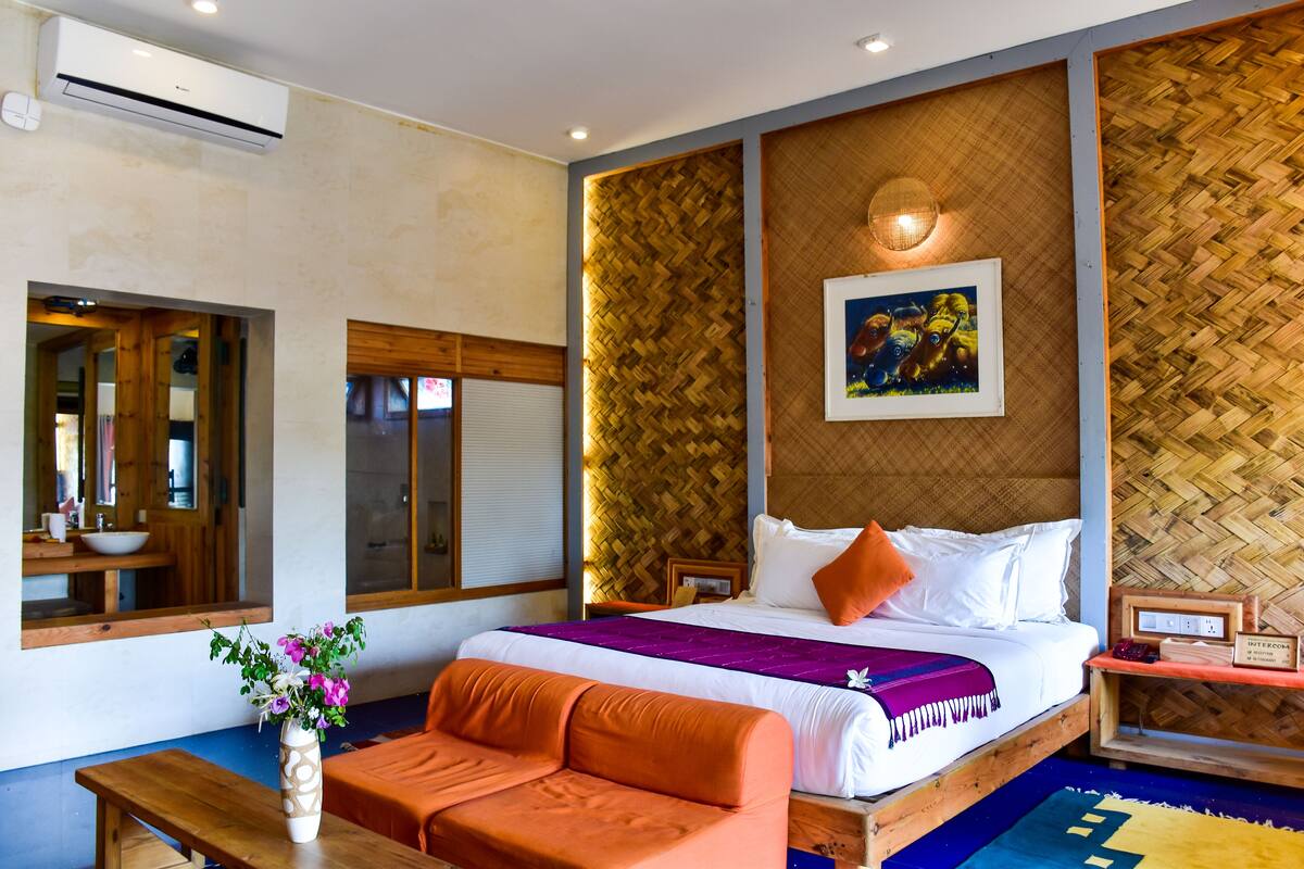 A hotel room with a bed, a wooden headboard, a wall-mounted picture, a bedside table, and a bench.
