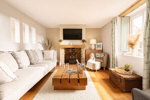 A cozy living room with a sofa, a coffee table, a fireplace, and a television. - Woodbine Cottage (Cheltenham)