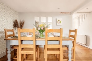A dining room with a wooden table and chairs, a vase of flowers, and a staircase in the background. - Woodbine Cottage (Cheltenham)