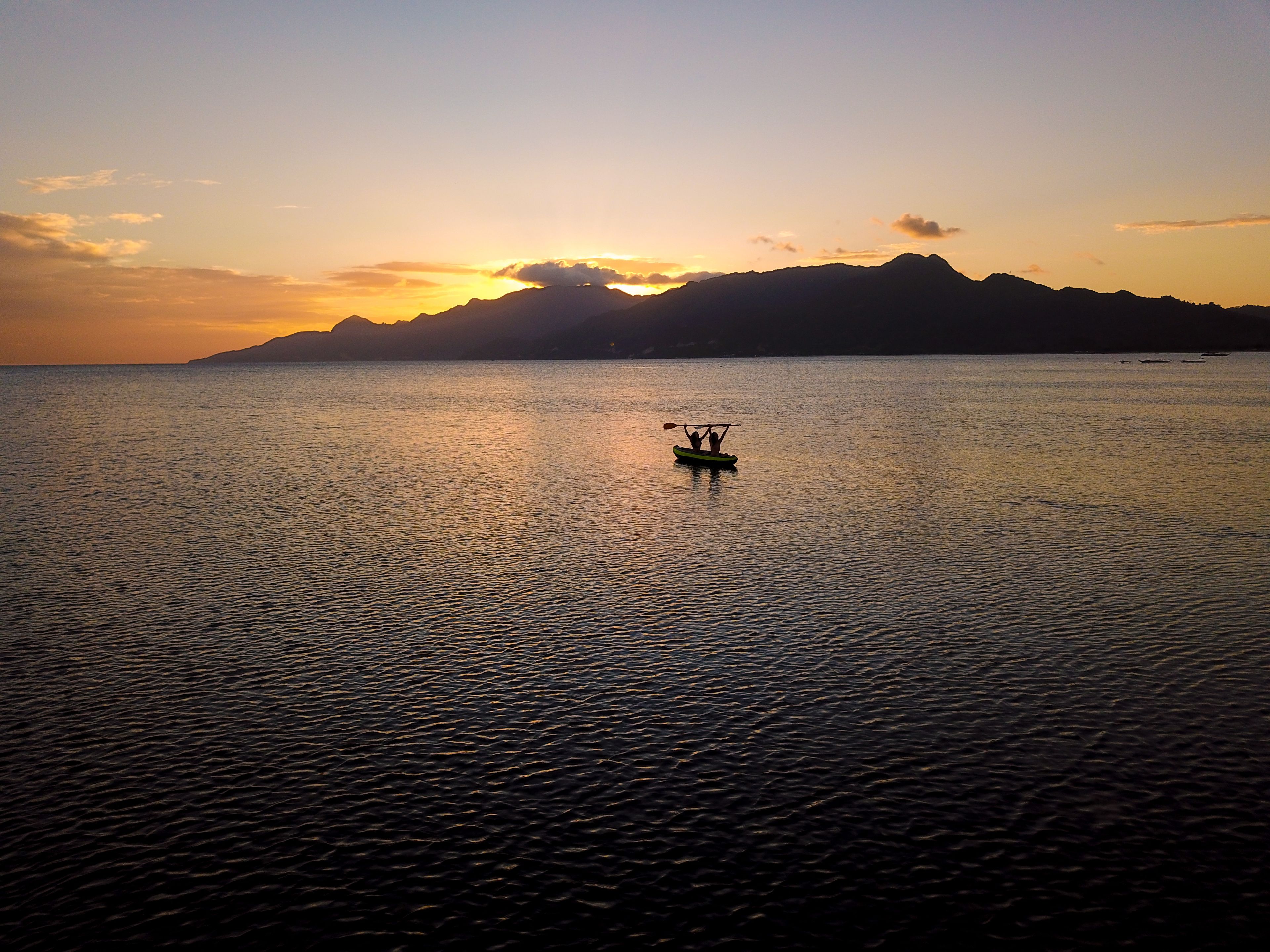 Un cuerpo de agua tranquilo con un bote que lleva a dos personas, rodeado de montañas y un atardecer.