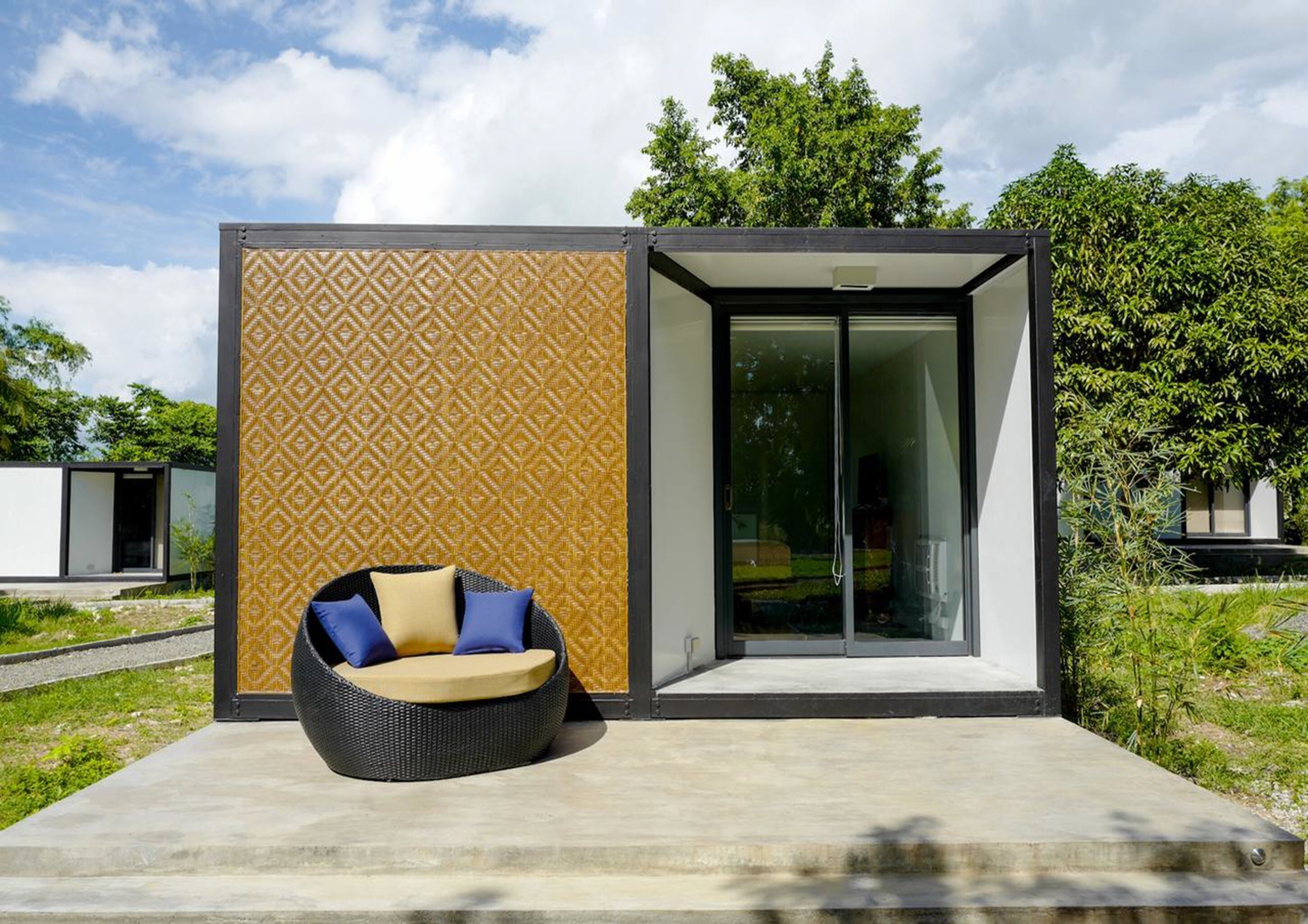 Un espace extérieur moderne, aménagé avec des sièges, un mur décoré de motifs et une entrée avec une porte en verre.