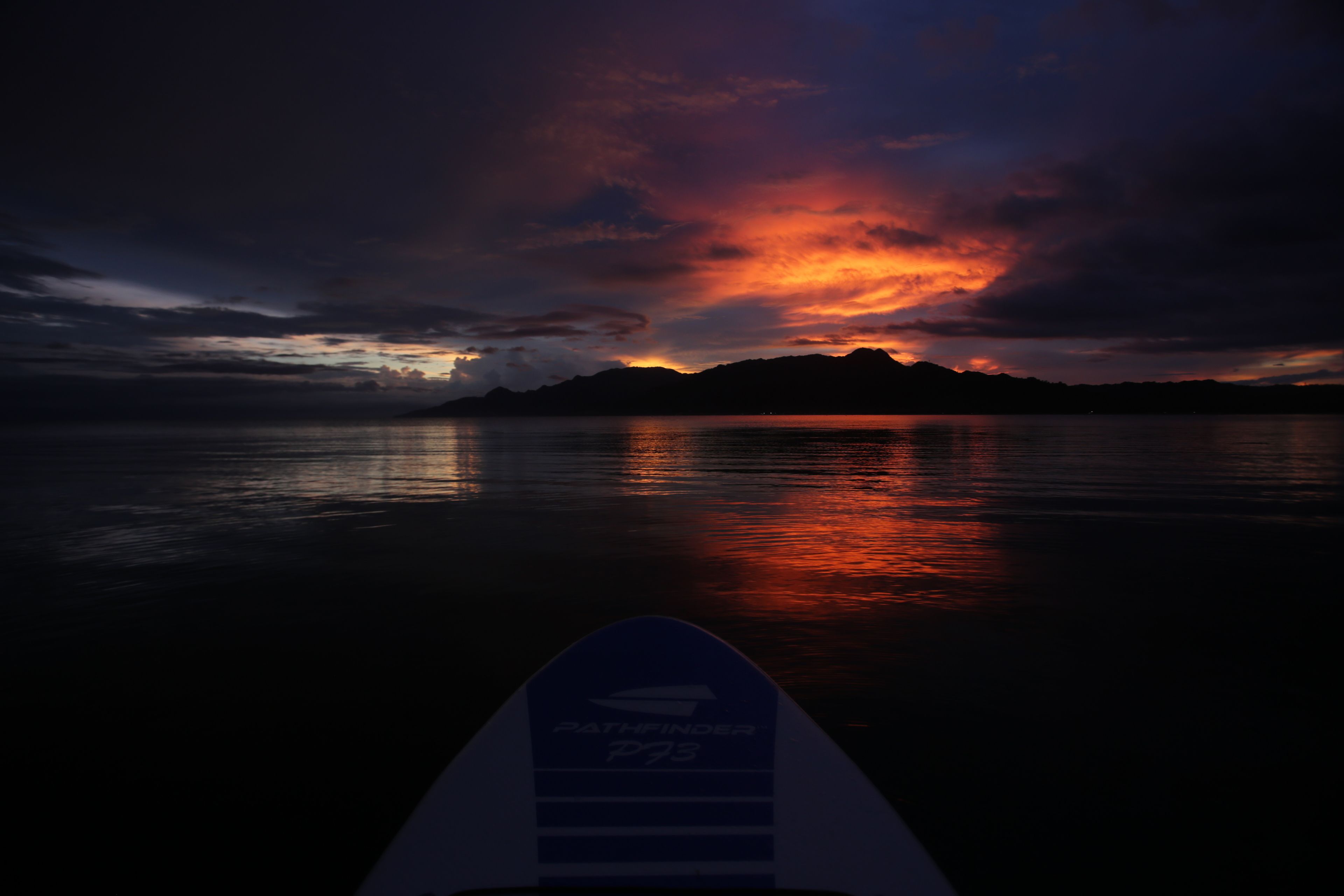 A surfboard with the text "Pathfinder P73" against a sunset over water.