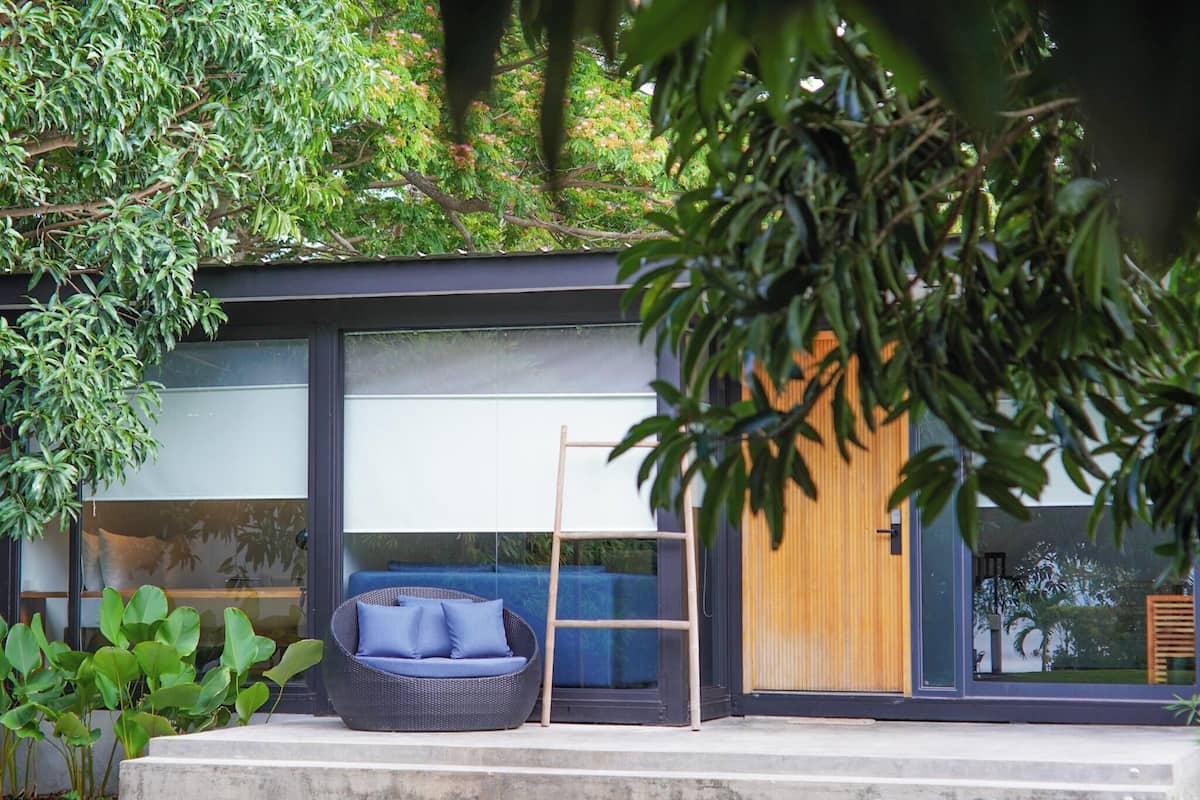 A modern house with large glass windows, a wooden door, and a blue outdoor seating area.