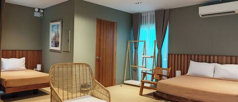 A hotel room with two single beds, a wicker chair, a wooden ladder, and a ceiling-mounted air conditioner.