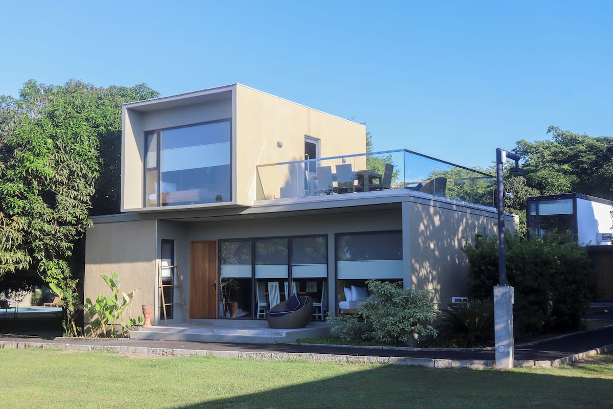 A modern two-story house with large windows, a balcony, and a well-maintained lawn.