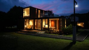 A modern house with a glass facade, a visible bedroom, and a well-lit entrance. - Cala Laiya (San Juan)