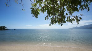 A beach with clear water, a sandy shore, and distant mountains. - Cala Laiya (San Juan)