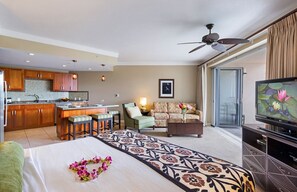 Habitación de hotel con kitchenette, comedor, sala de estar con sofá y televisión, y cama con colcha estampada.