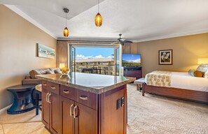 A hotel room with a large bed, a sofa, a dining area, and a view of the building. - Maui Resort Rentals: Honua Kai Hokulani 723 – Luxurious 7th Floor Oceanview Studio (Lahaina)
