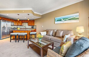 A modern kitchen with a central island, a dining area with a glass coffee table, and a living room with a sofa and a lamp. - Maui Resort Rentals: Honua Kai Hokulani 723 – Luxurious 7th Floor Oceanview Studio (Lahaina)