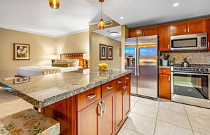A modern kitchen with a central island, stainless steel appliances, and wooden cabinetry. - Maui Resort Rentals: Honua Kai Hokulani 723 – Luxurious 7th Floor Oceanview Studio (Lahaina)
