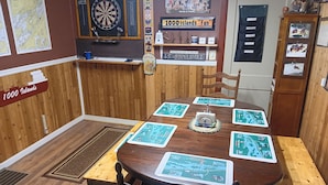 Ein Holztisch mit Karten und Dartscheibe, umgeben von Stühlen.