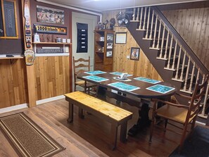 Une pièce chaleureuse avec un intérieur en bois, une table à manger avec des jeux de cartes, un banc, un escalier et divers éléments décoratifs sur les murs.