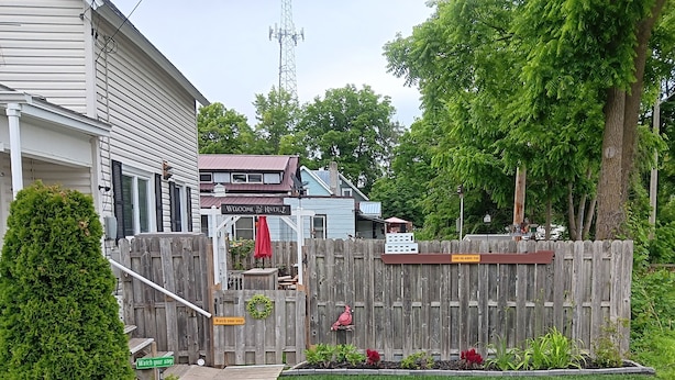 Ein umzäunter Garten mit einer Holzterrasse, einem Willkommensschild und einem Schild mit der Aufschrift 'Vorsicht, einsteigen'.
