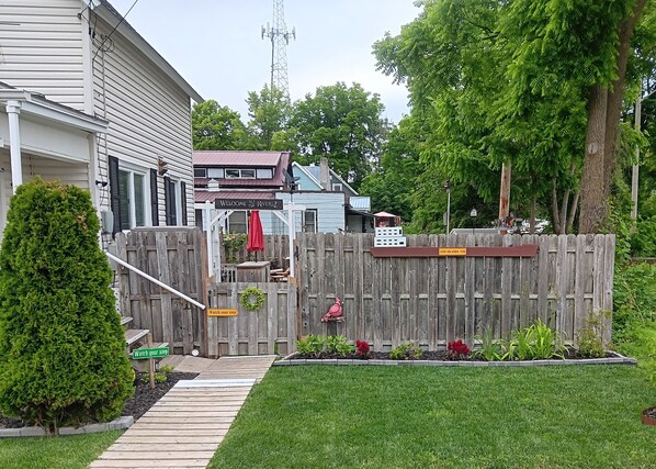 A fenced backyard with a wooden deck, a welcome sign, and a sign reading "Watch your step".