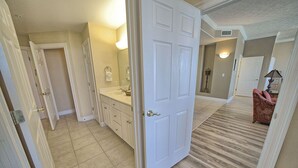 A hallway with a white door, a bathroom with a sink and mirror, and a red chair.