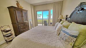 A bedroom with a large bed, a dresser, a chair, and a view of the outdoors.