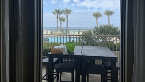 A balcony with a table, chairs, and a view of the ocean and palm trees.