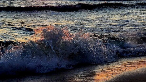 A sunset over the ocean with waves crashing onto the shore.