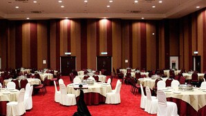 A large conference room with multiple round tables, white chairs, and red carpeting.